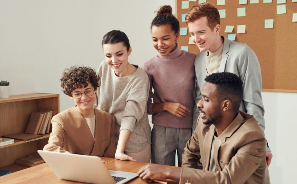 A team of young adults gathered around a laptop smiling